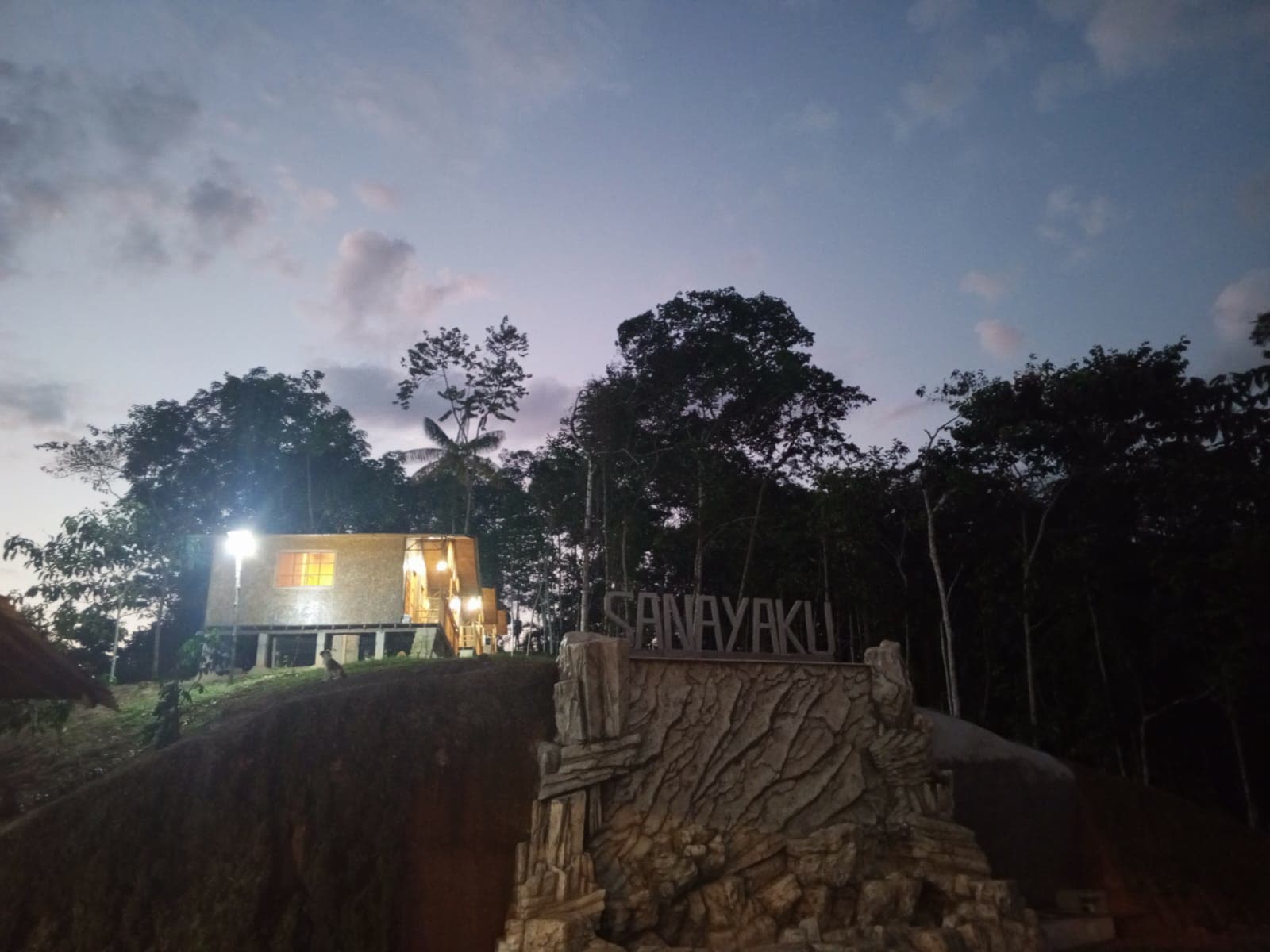 Letrero de Sanayaku y casa iluminada al anochecer