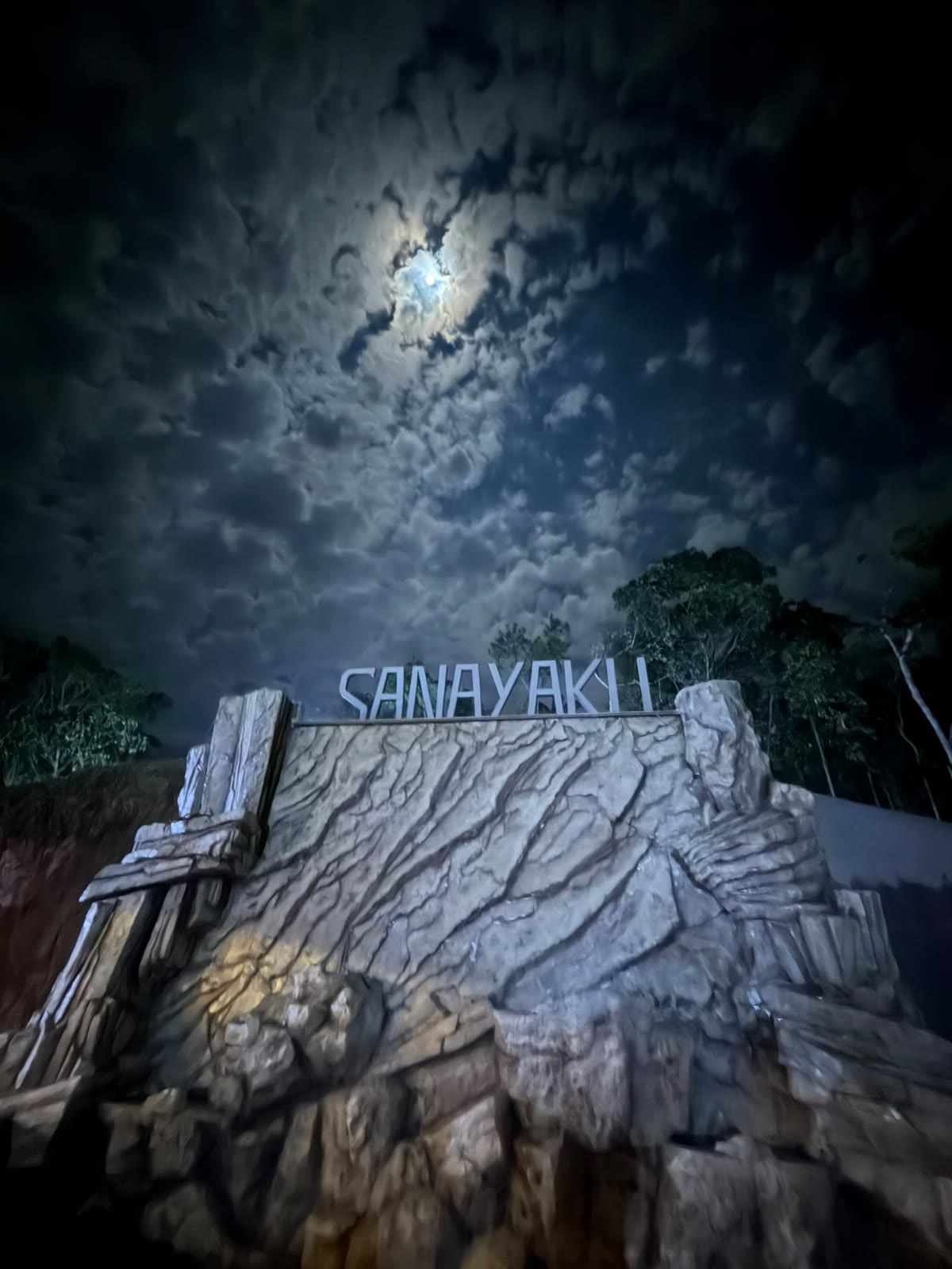 Letras de Sanayaku sobre un muro de roca bajo un cielo nocturno con luna